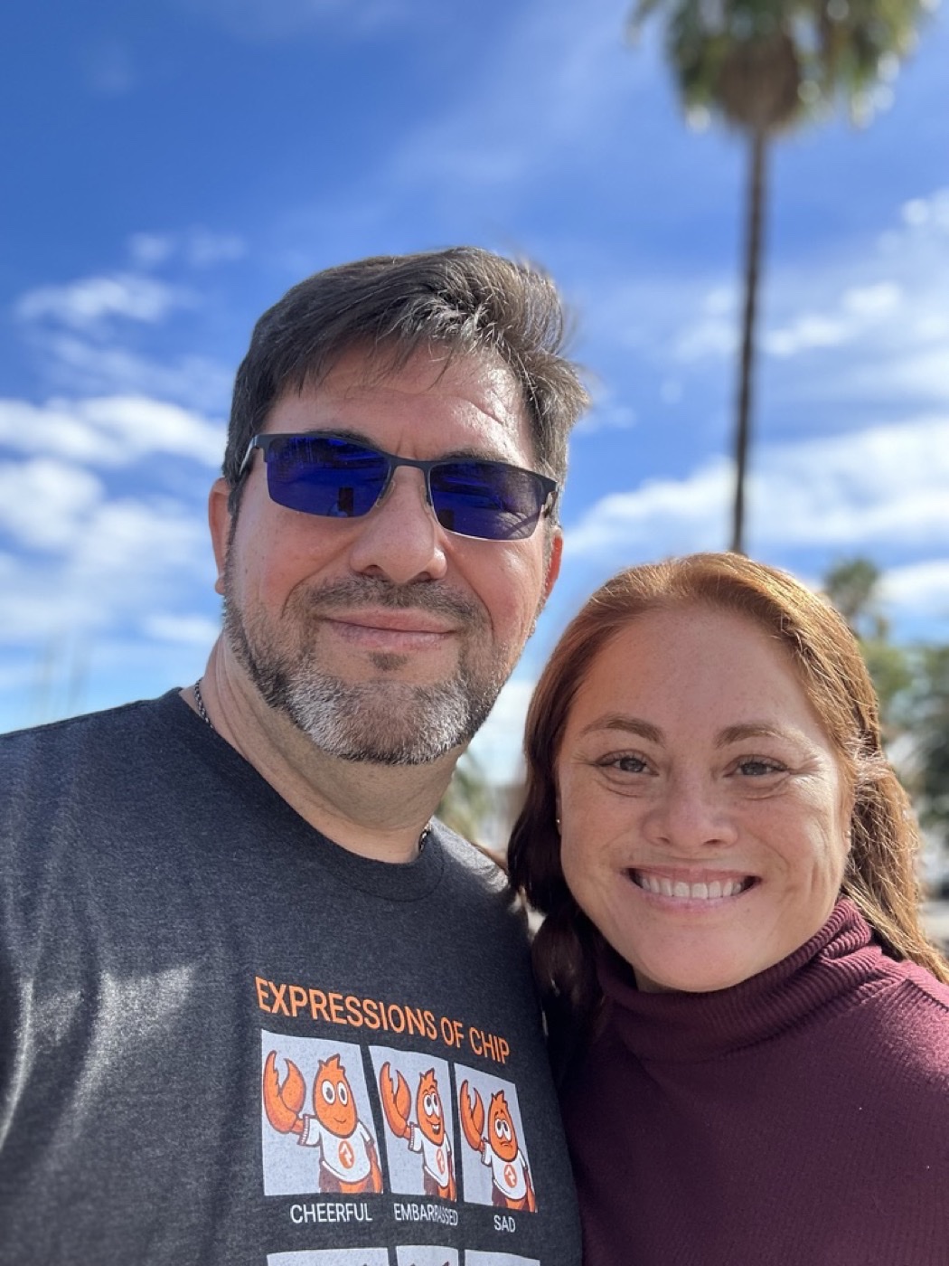 The hosts of Our House on Wheels — smiling outdoors under a blue sky
