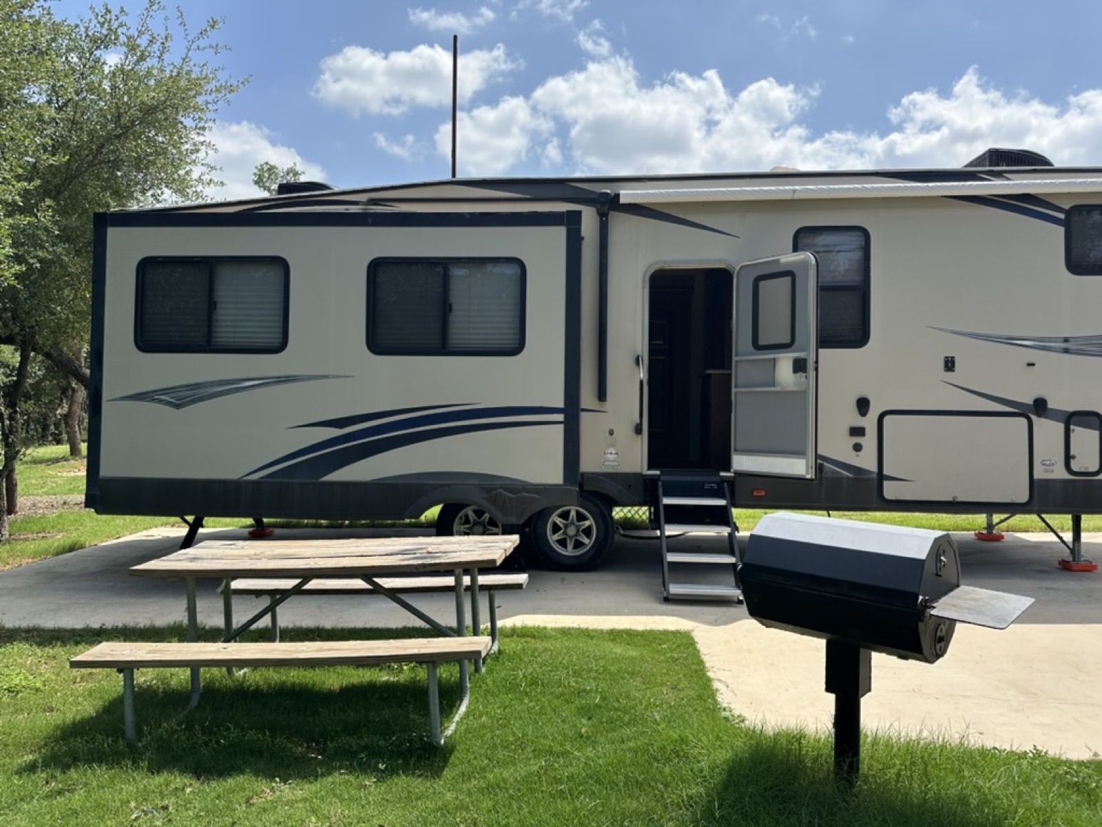 Campsite patio with picnic table and grill beside the fifth wheel entry