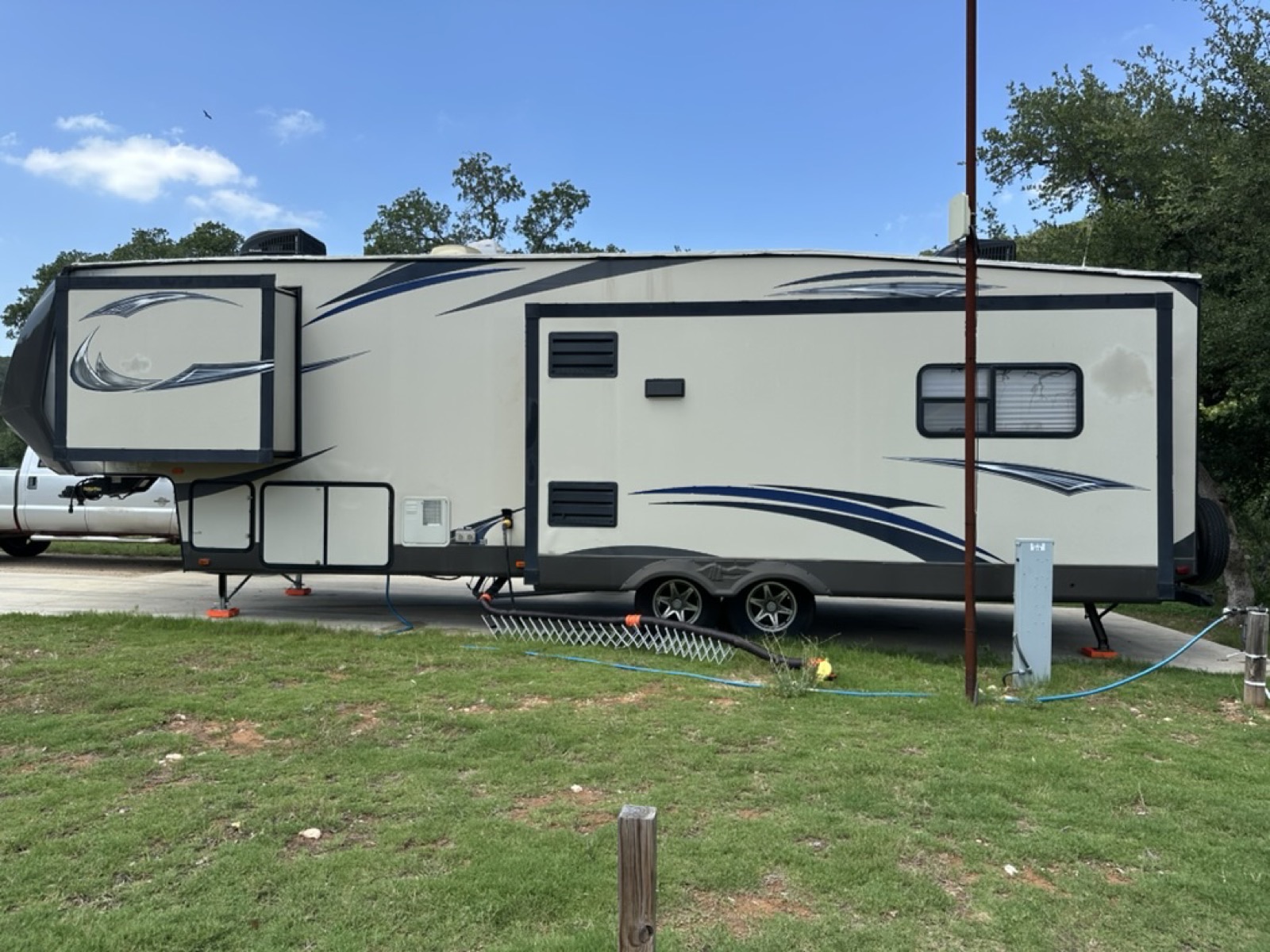 Fifth wheel with slides fully extended on a concrete campsite pad under a clear Texas sky